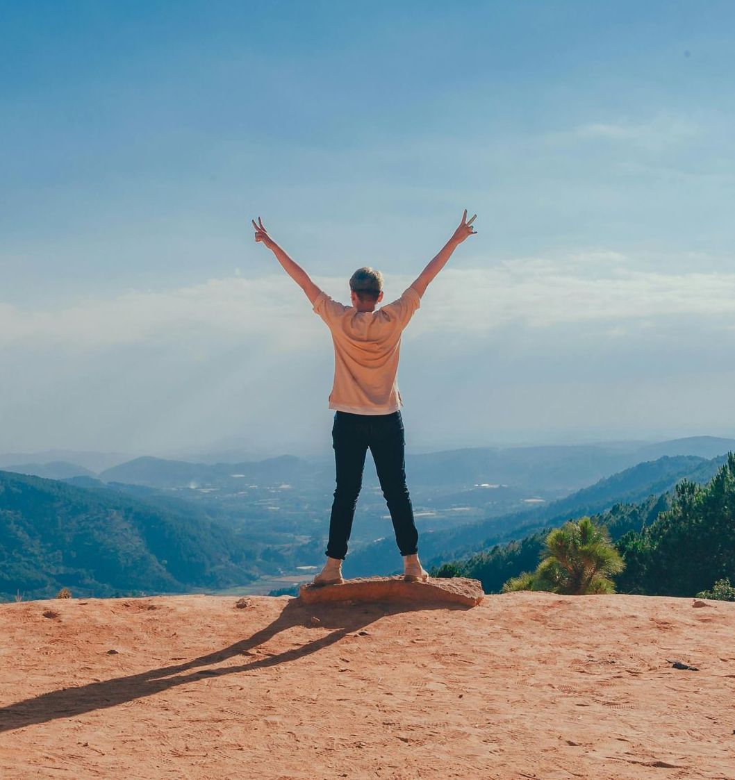 A woman is standing on top of a dirt hill with her arms outstretched.