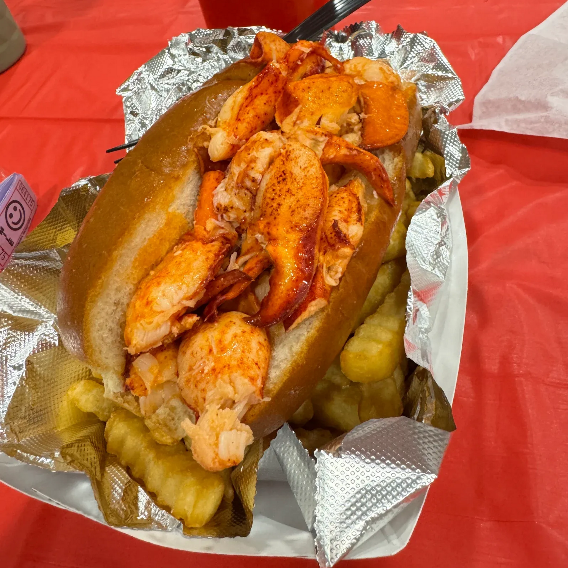 Lobster roll with fries in foil on a red tablecloth