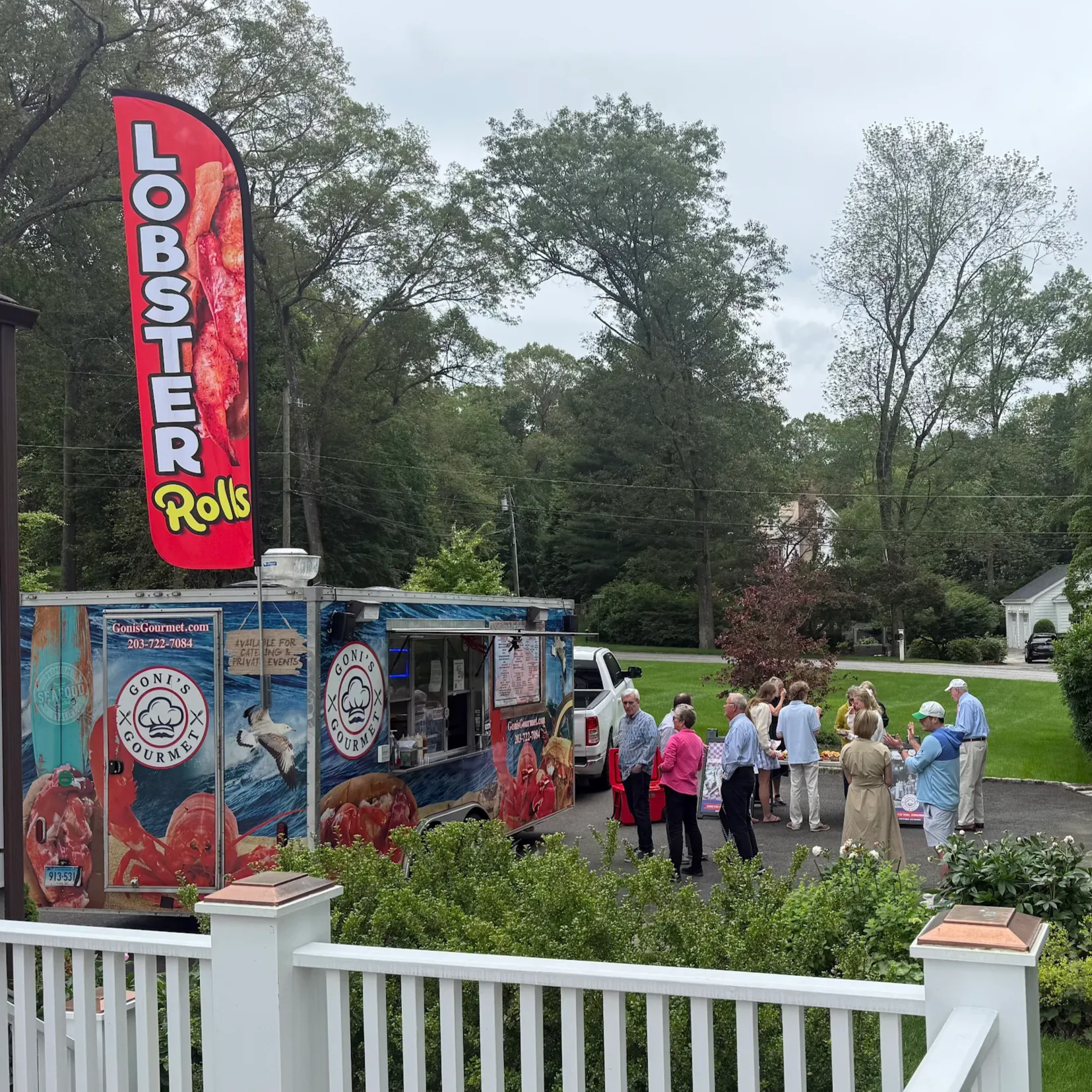 Lobster Rolls food truck parked by a fence with people gathered outside in a park setting
