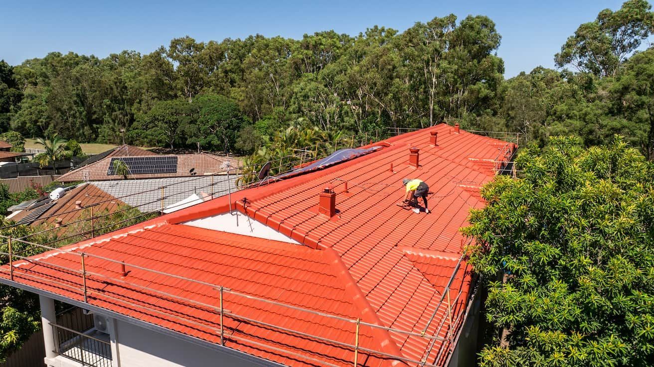 A man is standing on top of a red tiled roof.