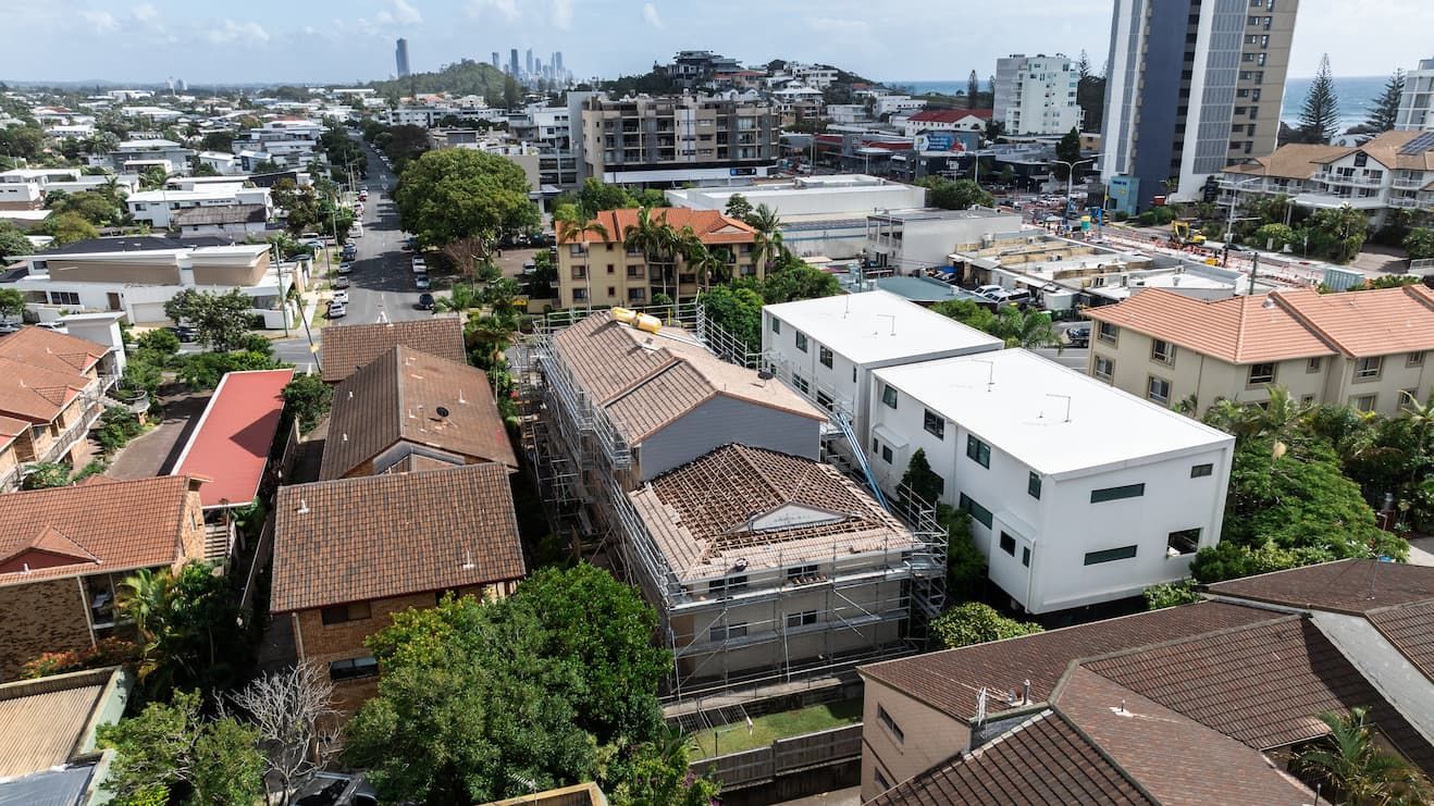Aerial view of a coastal neighborhood with houses, apartment buildings, and a structure under construction with a frame.