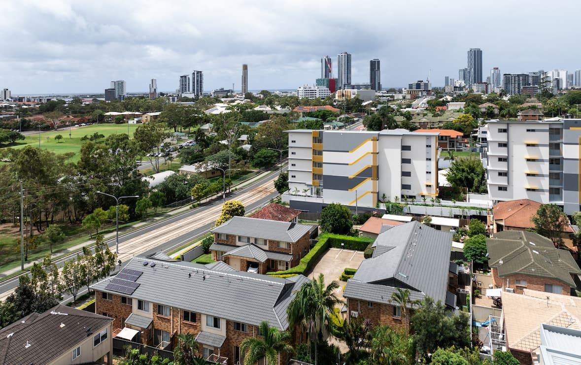 A suburban residential neighborhood with houses and apartment buildings, with a city skyline visible in the distance.