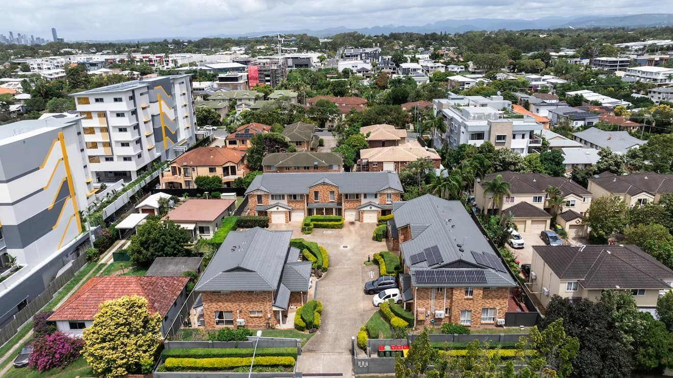 Aerial view of a residential apartment complex nestled in a suburban neighborhood with various buildings and lush trees.