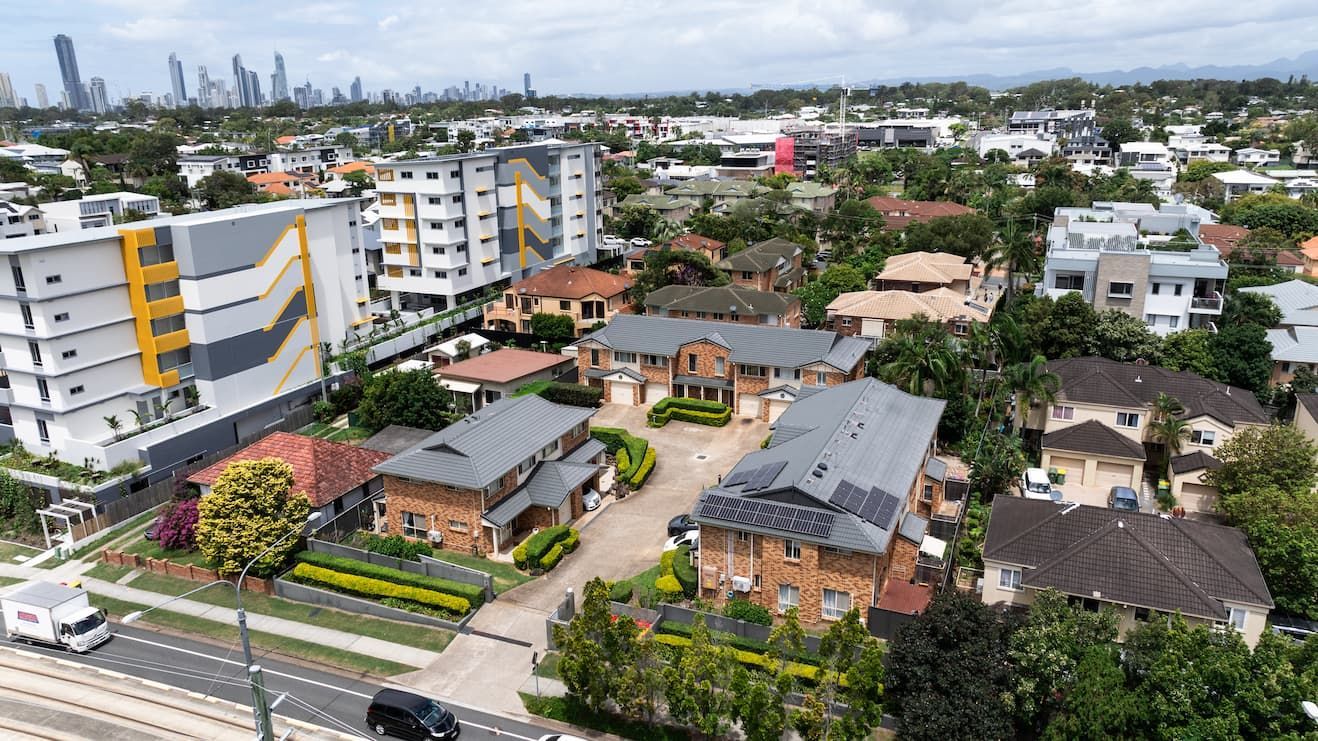 Aerial view of residential townhouses with a multi-story apartment building and distant city skyline in the background.