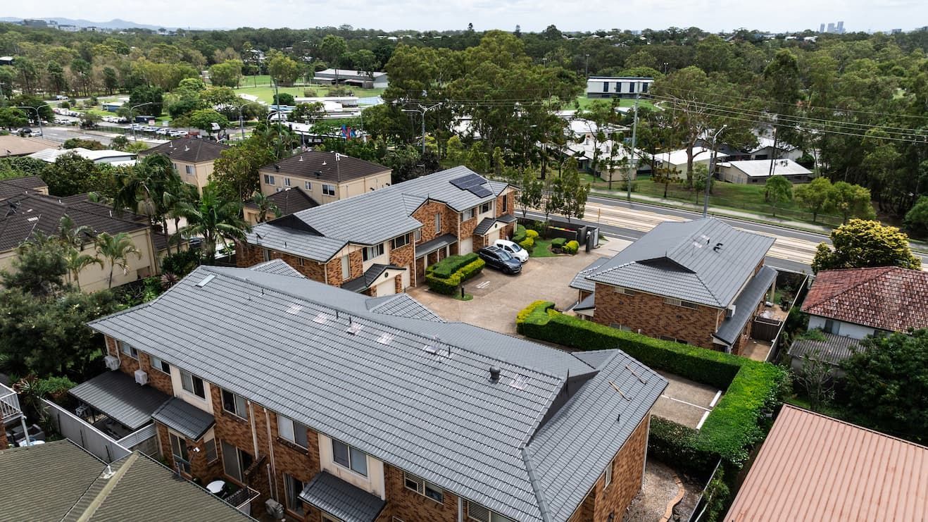 Aerial view of a residential townhouse complex featuring brick walls, grey tiled roofs, and lush surrounding greenery.