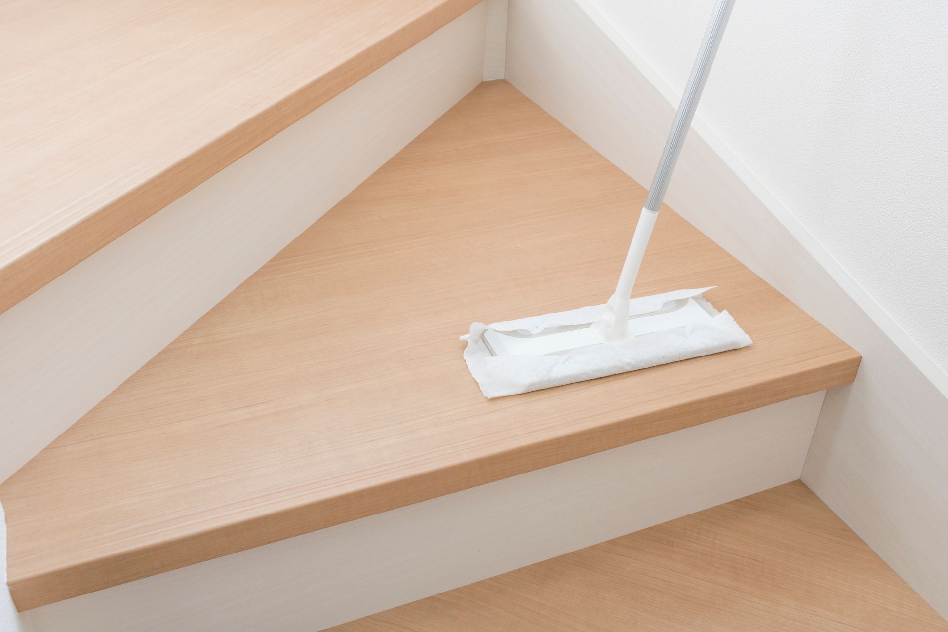 A mop cleaning a light-colored wooden staircase with white risers.