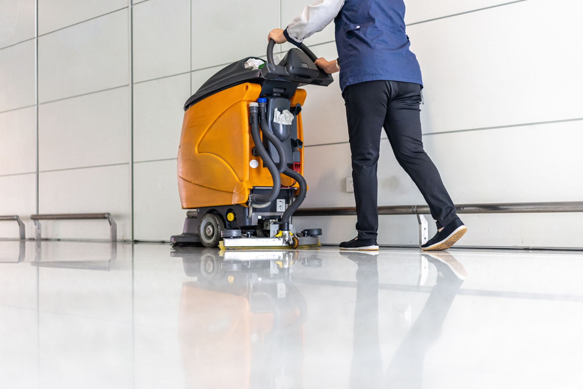 Person using a floor buffer to clean a tiled hallway.