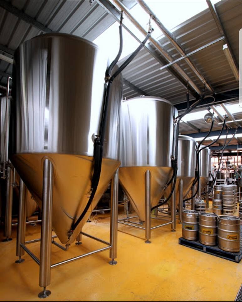 Stainless steel beer fermentation tanks in a brewery, with kegs on a pallet.