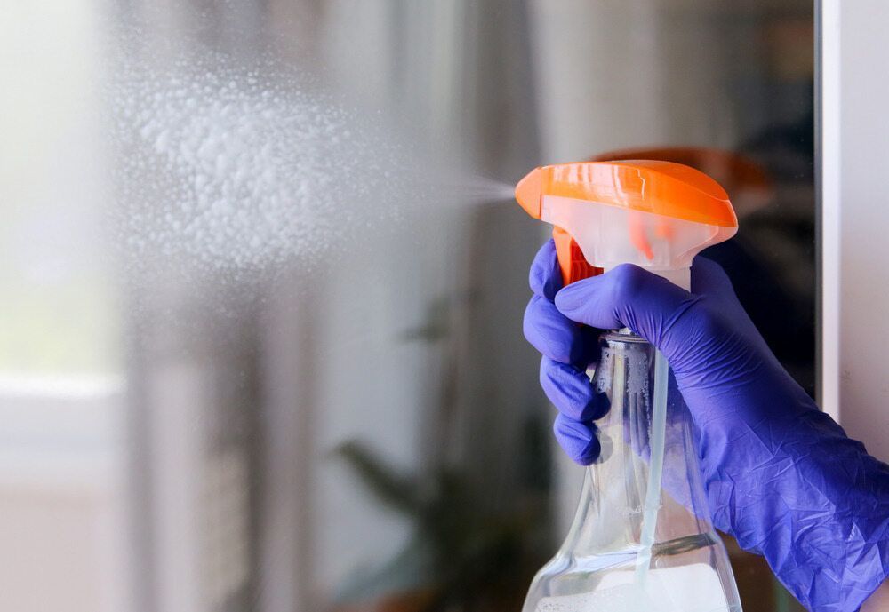 Person wearing yellow gloves using a red-handled squeegee to clean a window, blurred green background.
