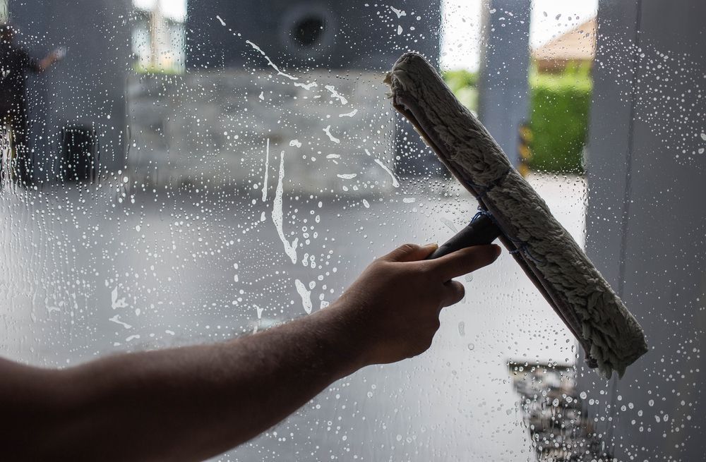 Hand using a squeegee to clean a window covered in soapy water.