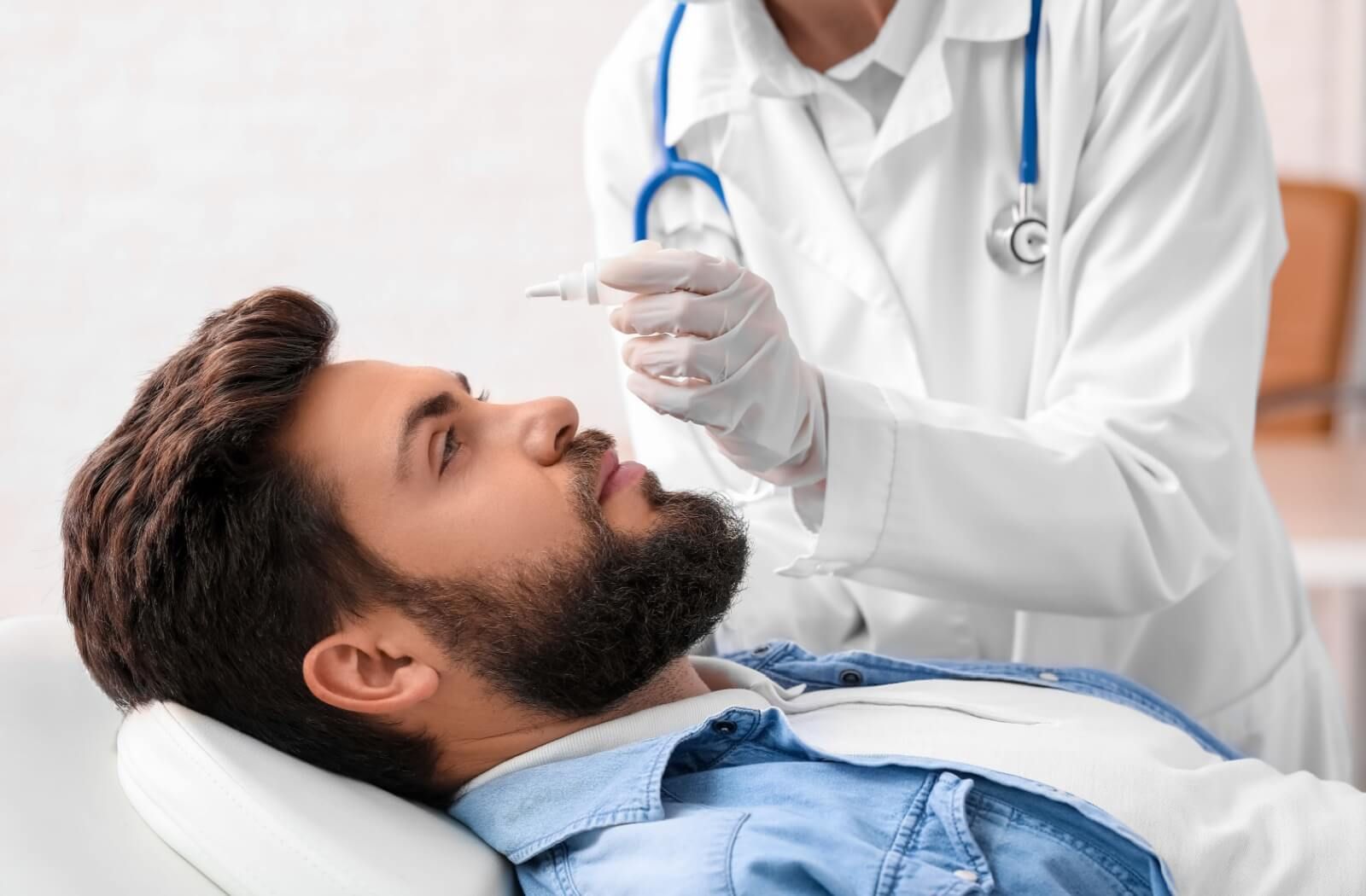 Doctor in gloved hands placing drops in a man's eyes representing dry eye treatment