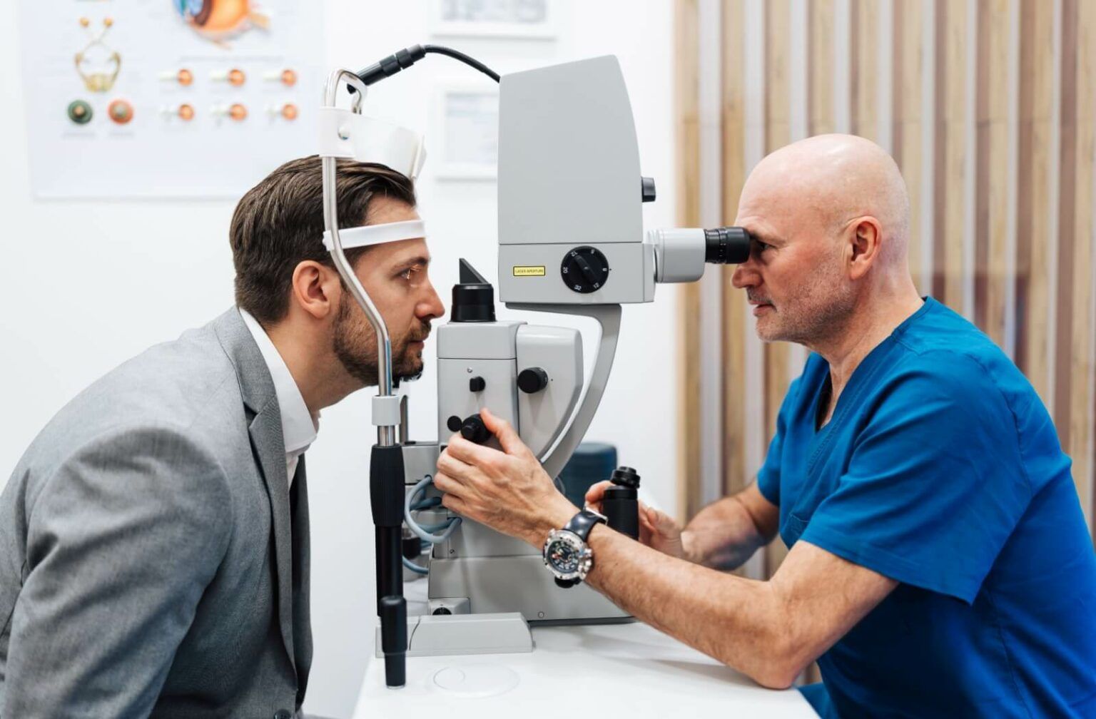 Doctor in blue scrubs and a man in a gray suit, representing the concept of How long does an eye exam take.
