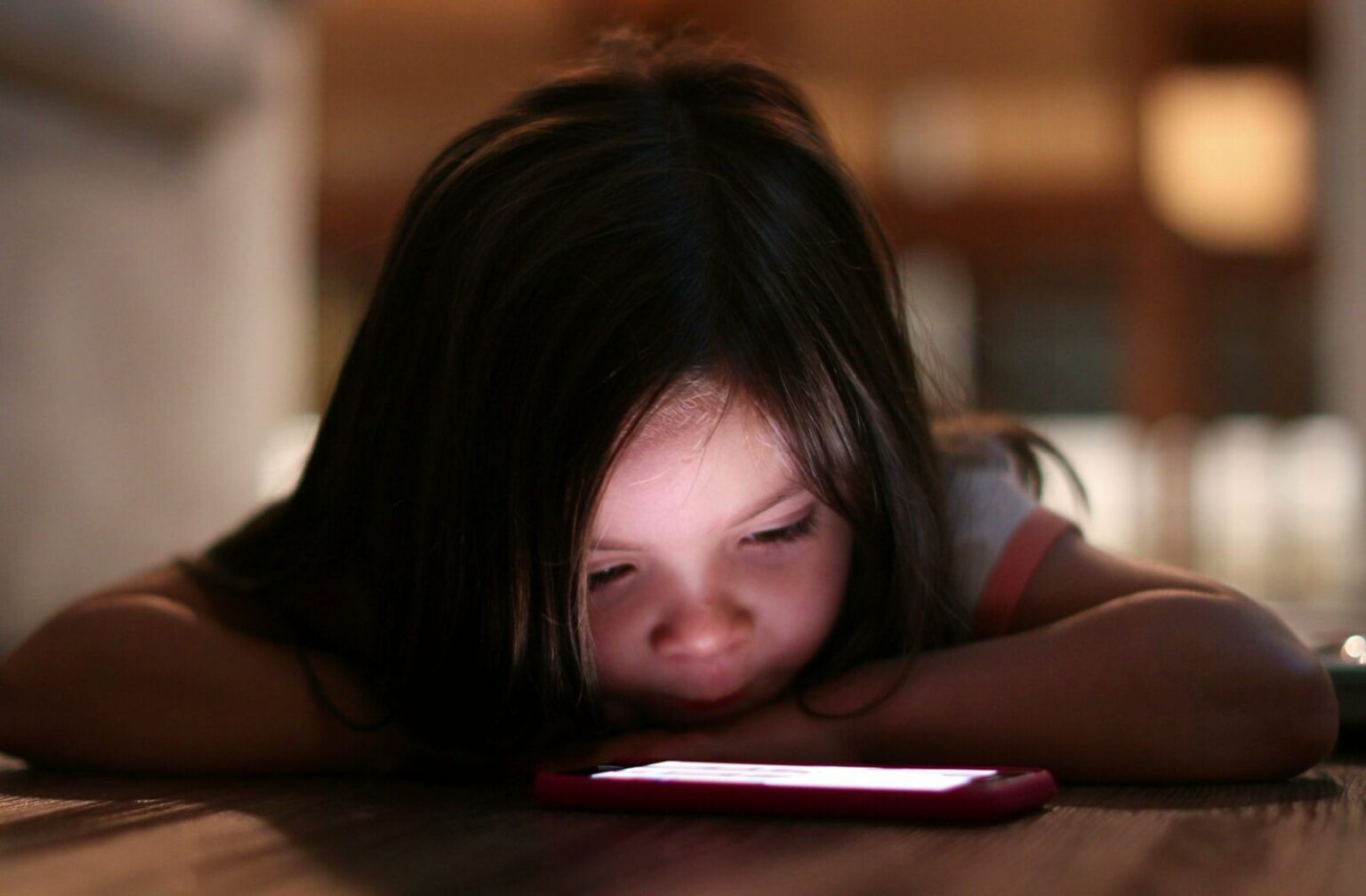 Image of a child looking closely at a phone screen in the dark represetning what causes myopia to worsen