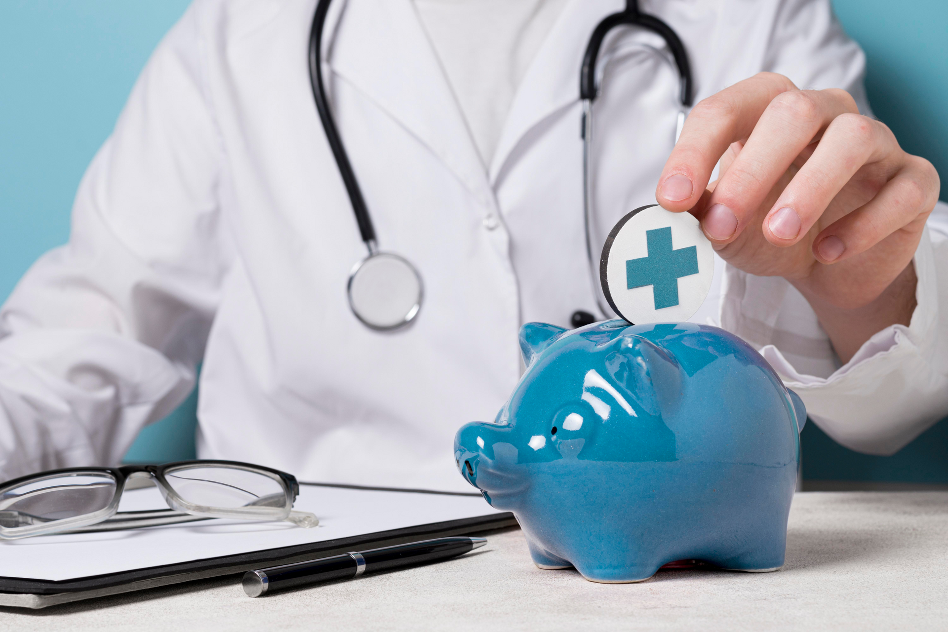 A close up shot of a doctor putting a coin with a blue cross symbol inside a blue piggy bank.