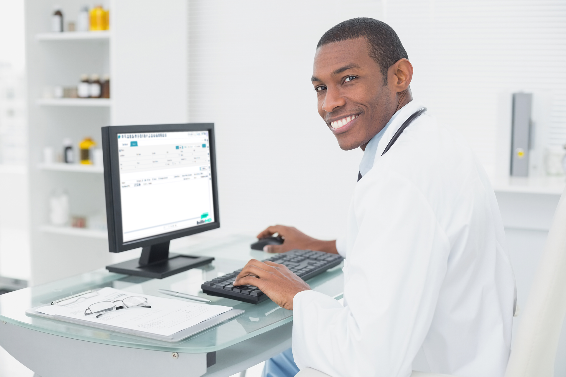 An African American doctor smiling while sitting in front of a computer and using his medical billing software.