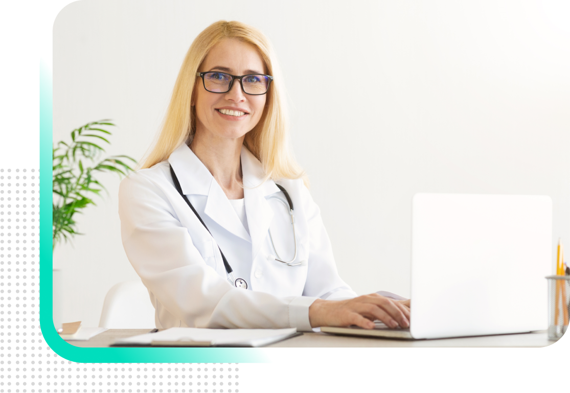 A female doctor is sitting at a desk using a laptop computer.