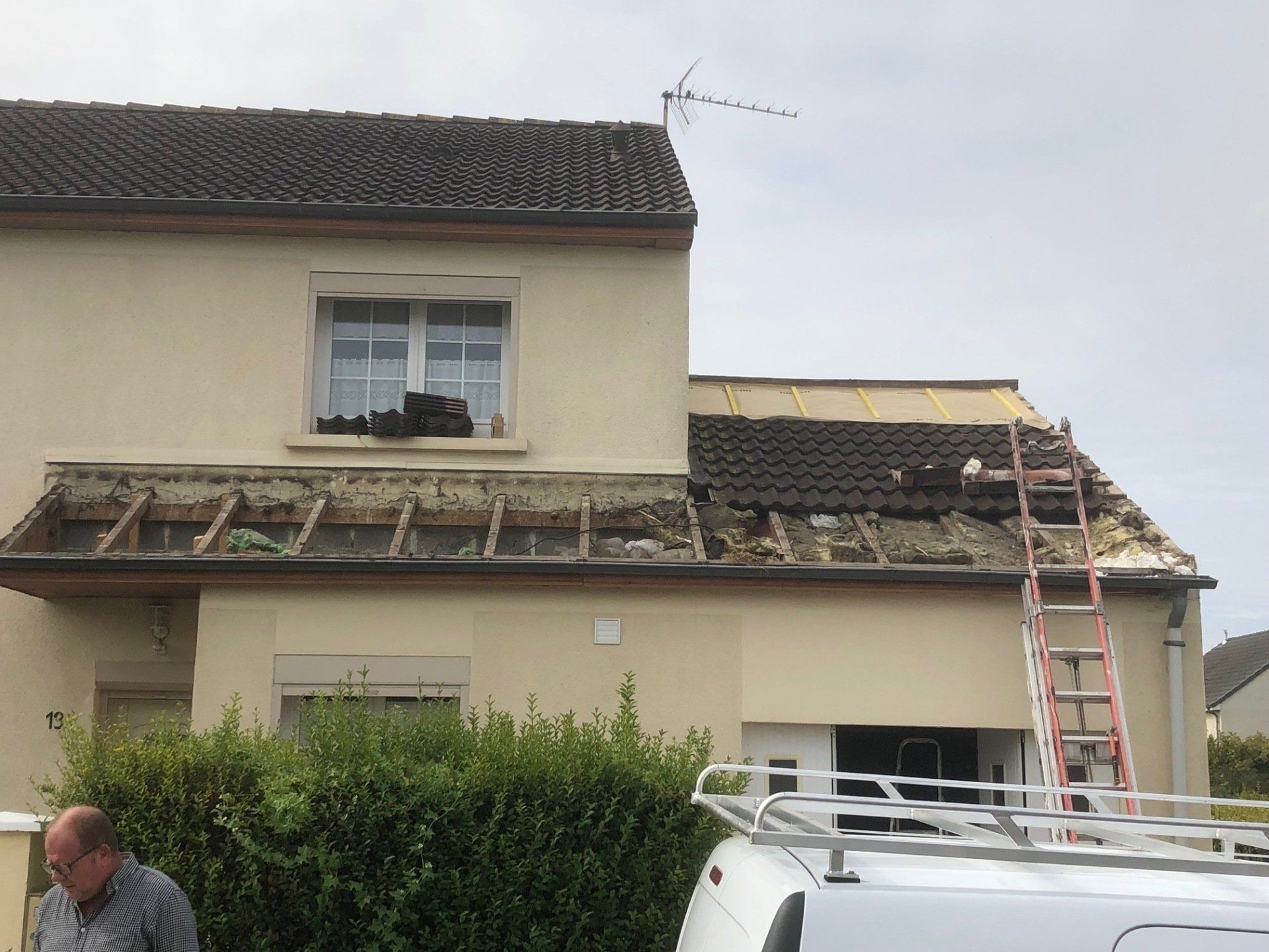 Un homme se tient devant une maison avec une échelle sur le toit.