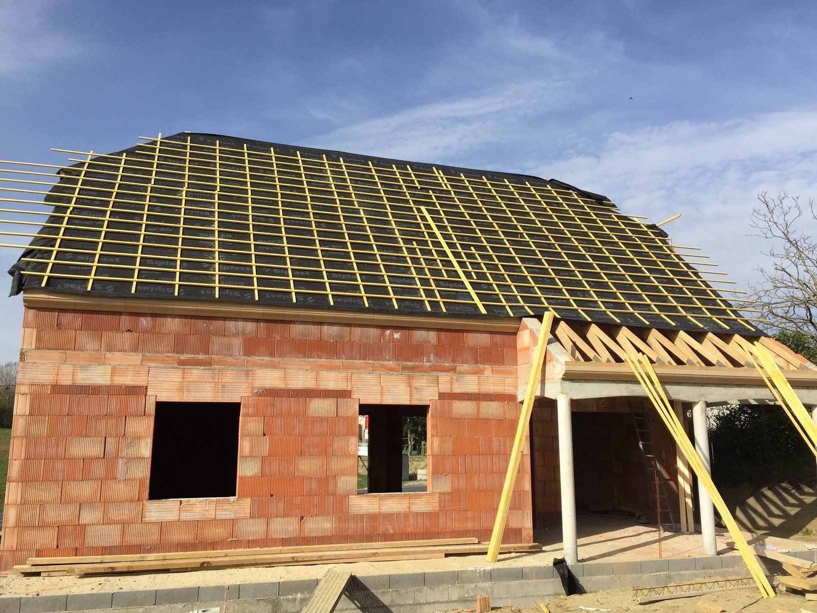 A brick house under construction with a roof that is being built.