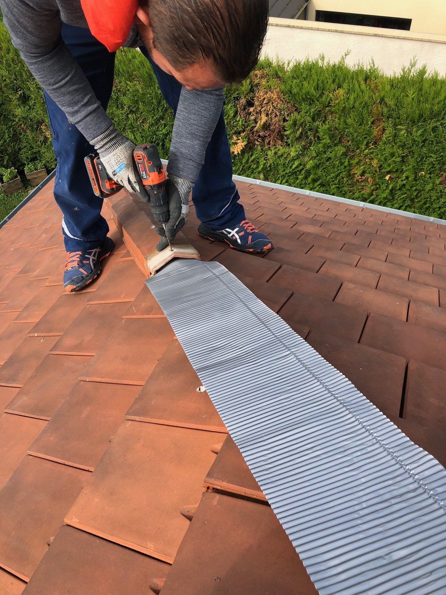 Un homme travaille sur un toit avec une perceuse.