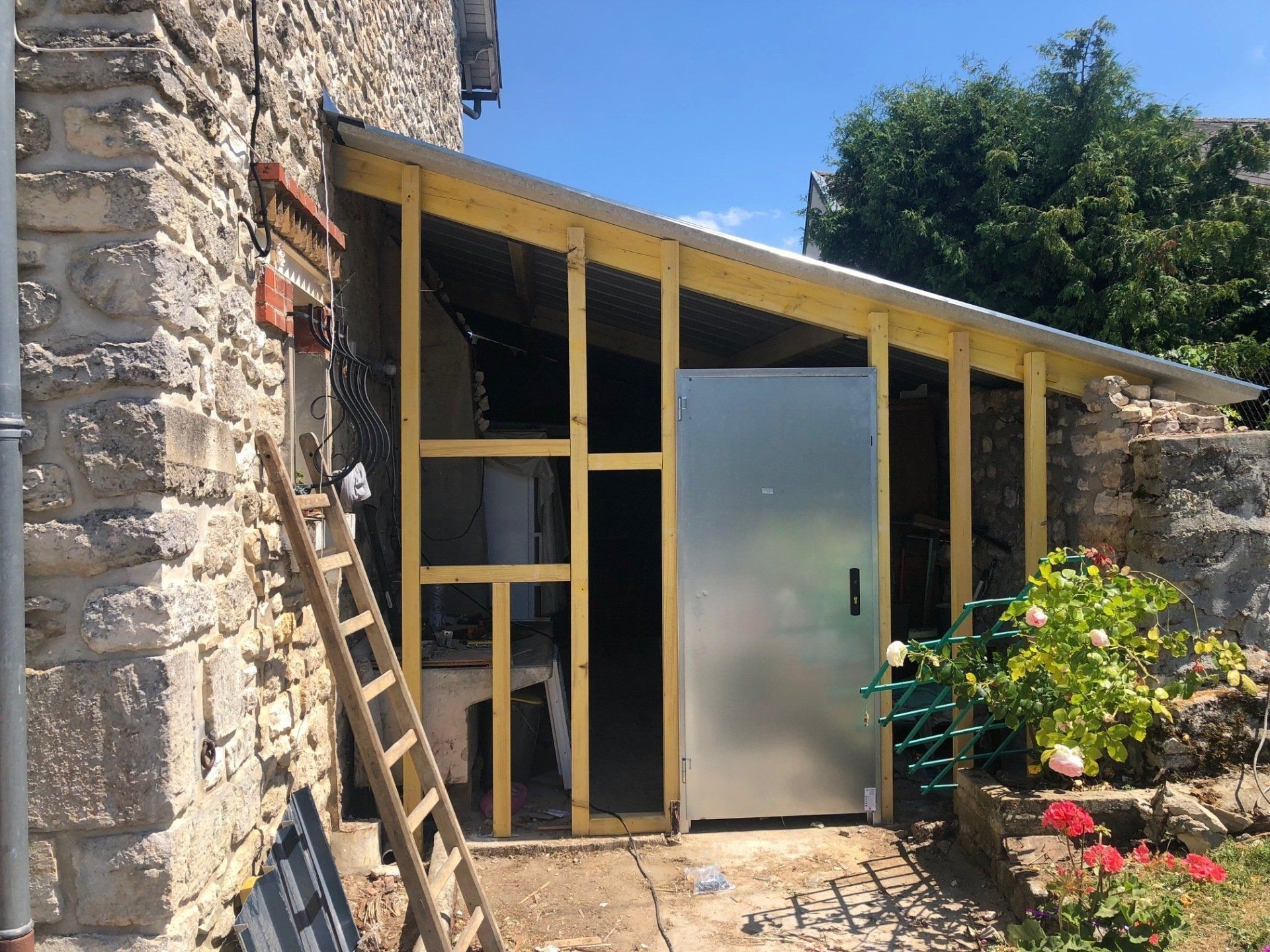 Un hangar en bois est en cours de construction à côté d'un bâtiment en pierre.