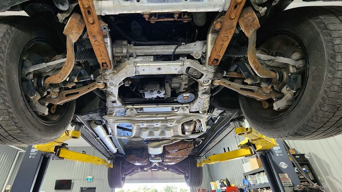 Undercarriage of a vehicle on a lift, showing rusty suspension components and engine.