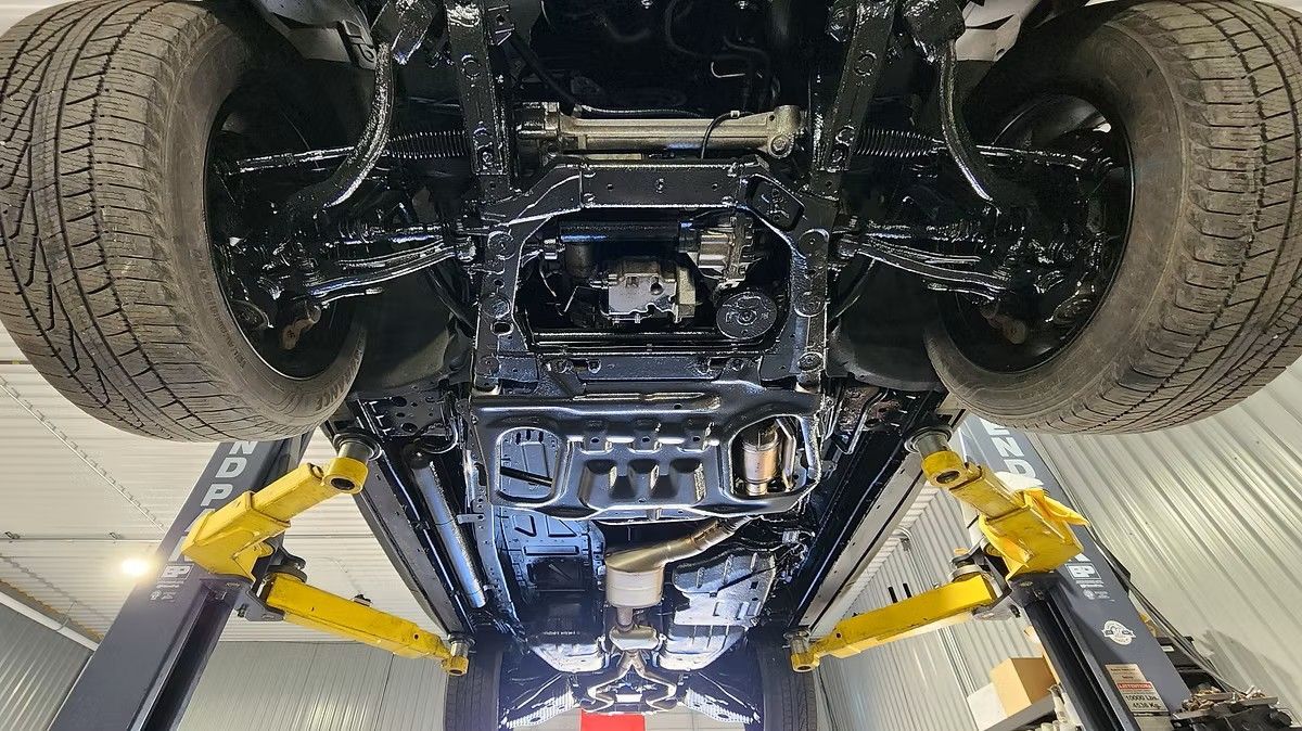 Underside of a black vehicle on a yellow lift in a garage, with tires visible.