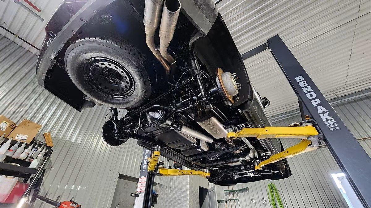 Black car raised on a yellow lift in a garage. Underside visible, with shiny black coating.