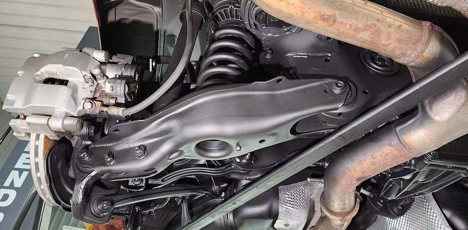 Underside of a vehicle showing suspension components: shock absorber, control arm, brake caliper, and exhaust pipe.