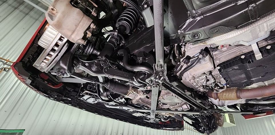 Underside of a car being worked on, showing engine components and protective coating applied.