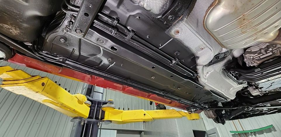 Undercarriage of a vehicle lifted on a yellow car lift, red support rail visible, interior of a garage setting.