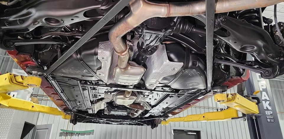 Underside of a car on a lift, showing exhaust system and undercarriage components.