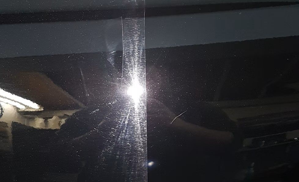 Black car paint, half polished, showing scratches and a bright reflection.