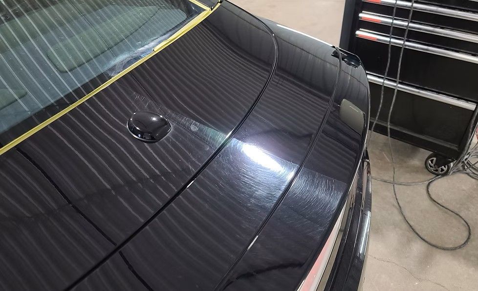 Black car hood with shiny finish, masking tape, in a garage with a tool chest.
