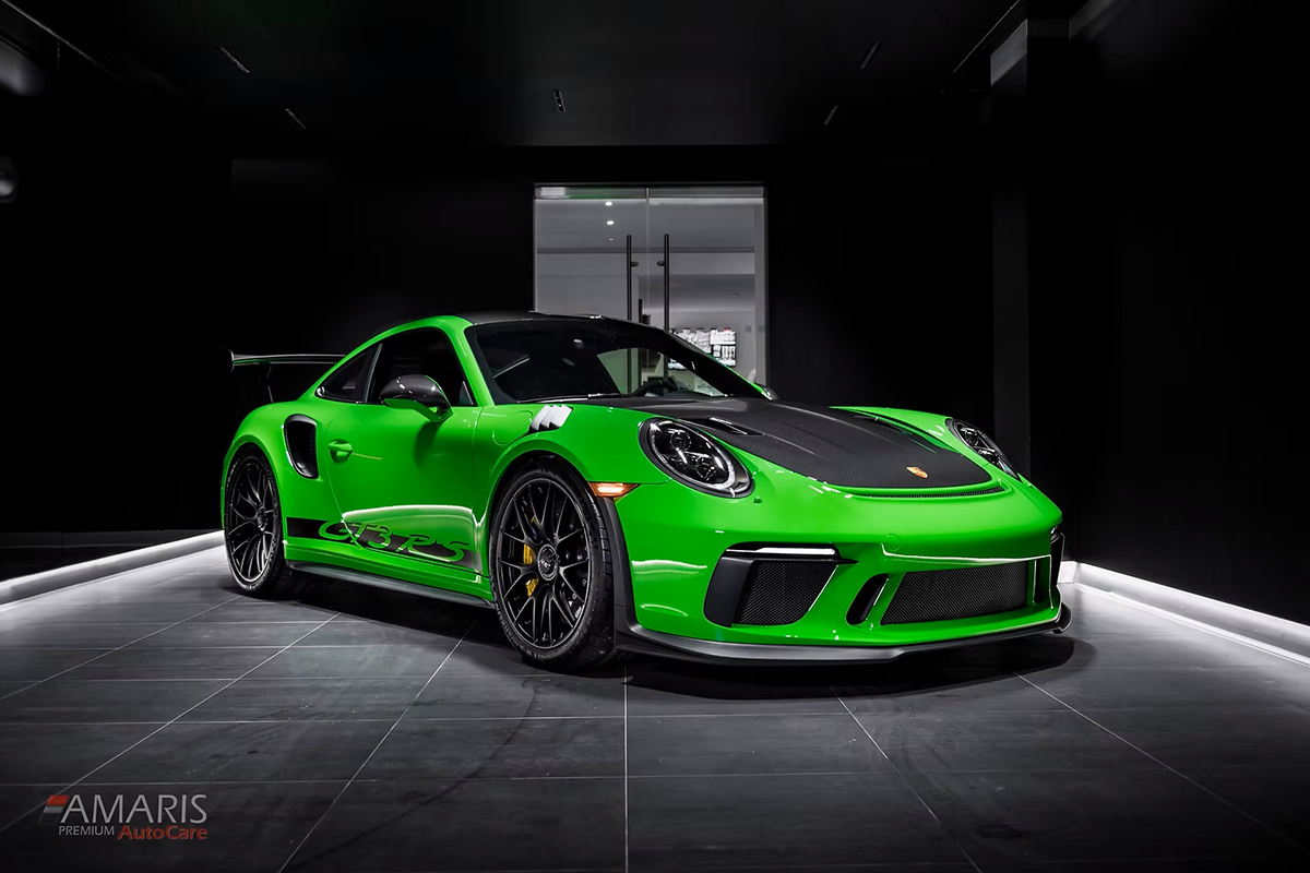 Green Porsche 911 GT3 RS sports car with black accents, parked in a dark showroom.