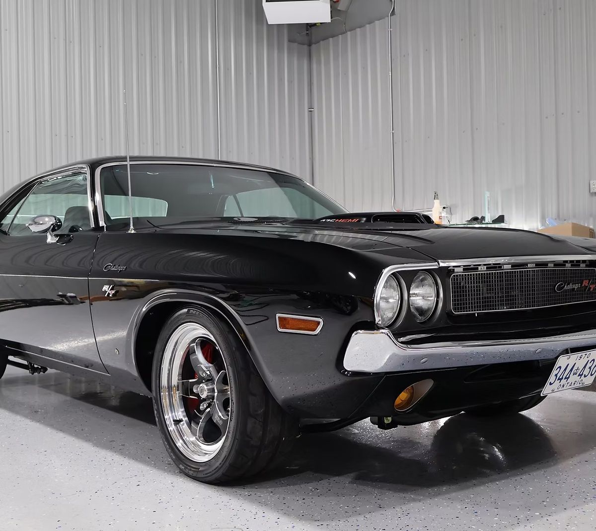 Black Dodge Challenger muscle car, parked inside a garage with gray walls and concrete floor.