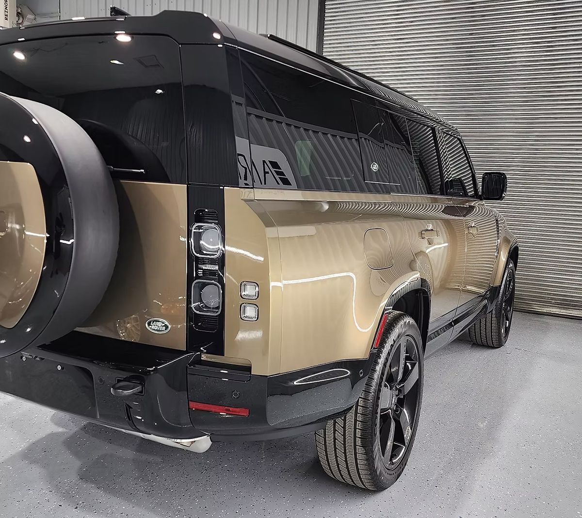 Gold Land Rover Defender SUV, black accents, spare tire on back, parked indoors.