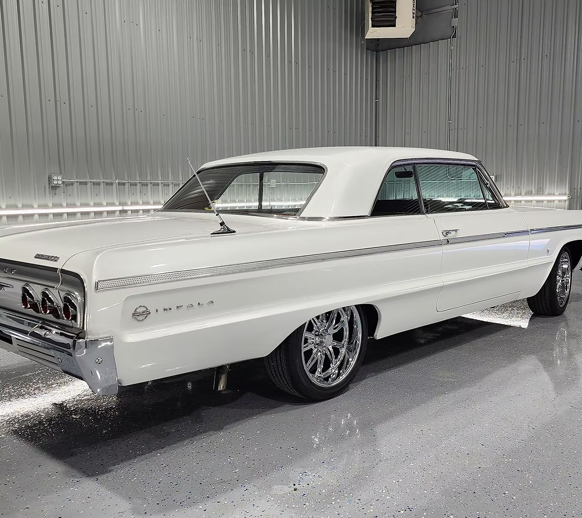 White 1964 Chevrolet Impala coupe, chrome accents, parked inside a garage, with chrome wheels.