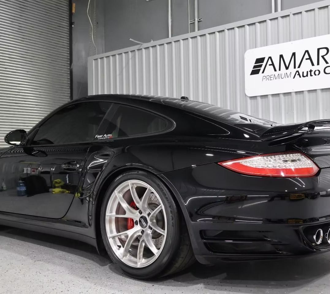 Black Porsche sports car with tinted windows, red brake calipers, and a spoiler, parked inside a garage.