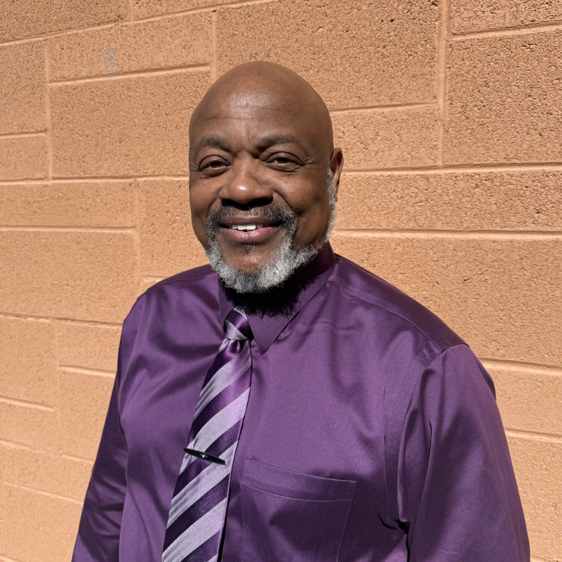 Woman smiling, wearing a black and white houndstooth jacket and floral top, against a purple background.