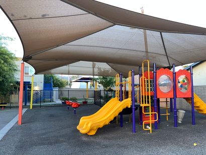 Two-story beige building with dark trim, trees, a fence, and a sign on a sunny day.