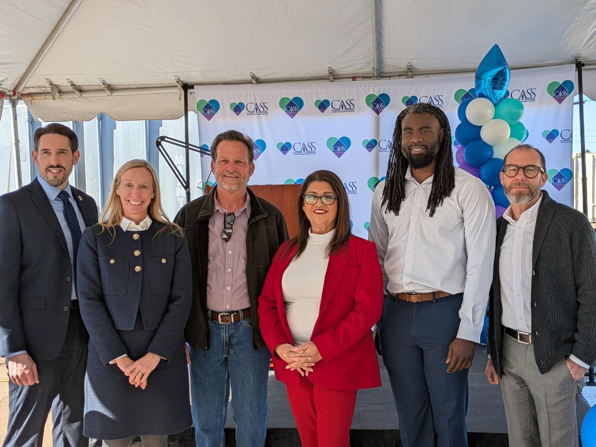 Group of people in business attire at an outdoor event with balloons and logos.