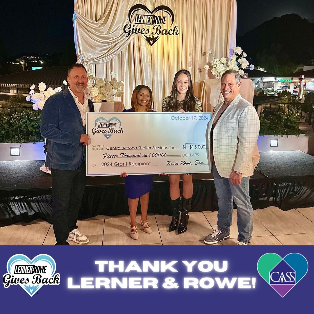 Lerner & Rowe present a large check to an organization. Four people pose outdoors at night.