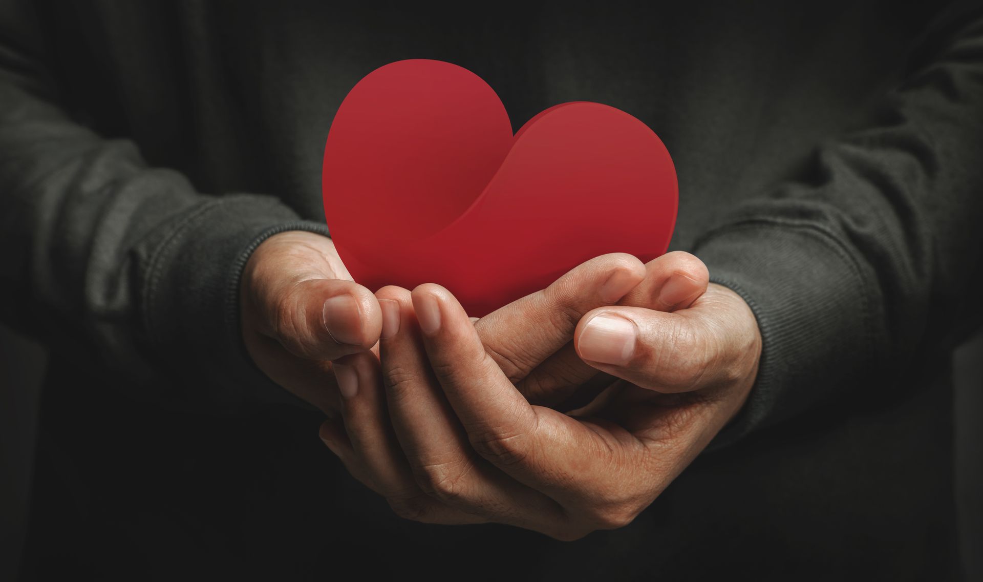 Hands cupping a red heart, offering care and love.