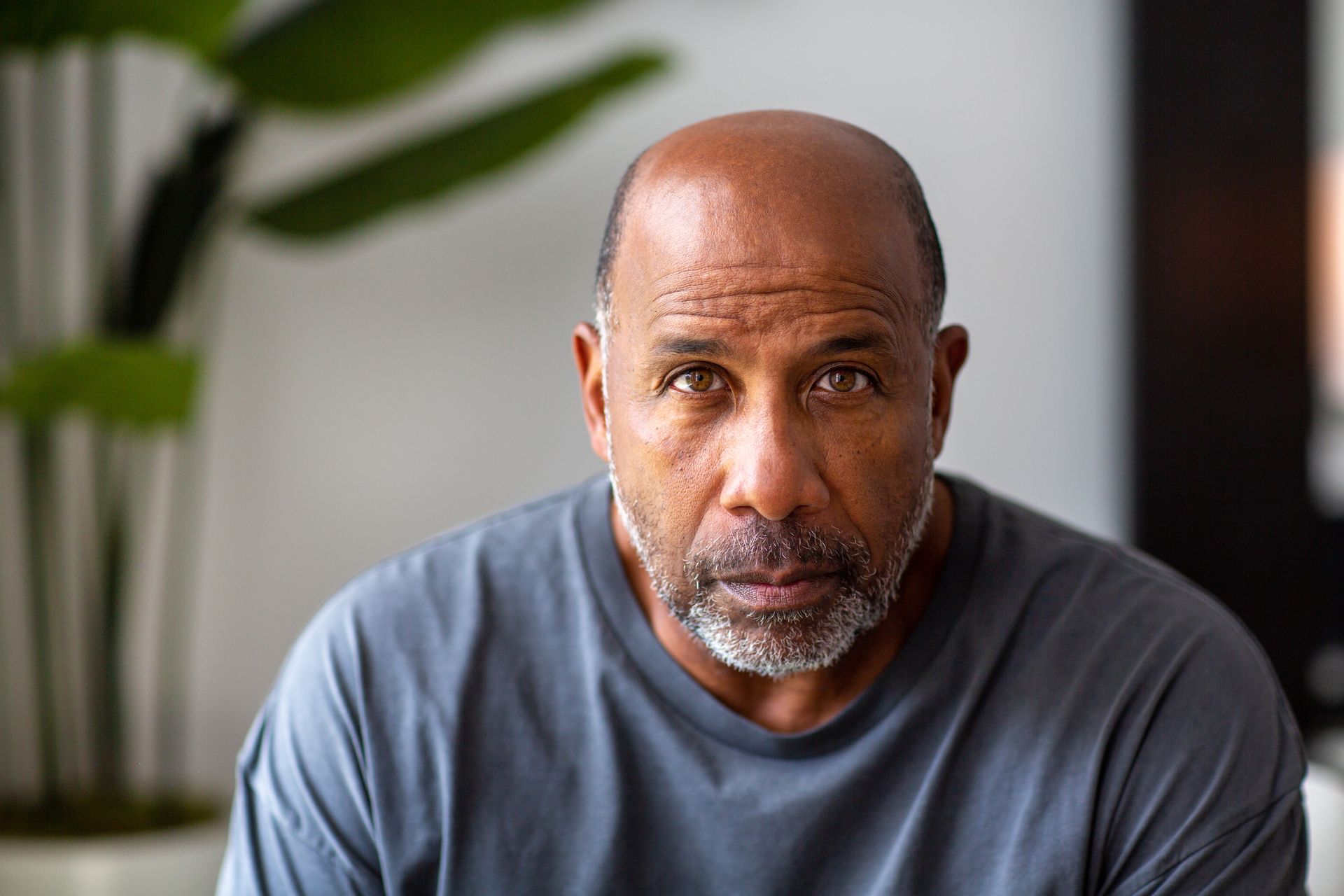 Bald Black man with a graying goatee, looking directly at the viewer, wearing a gray shirt.