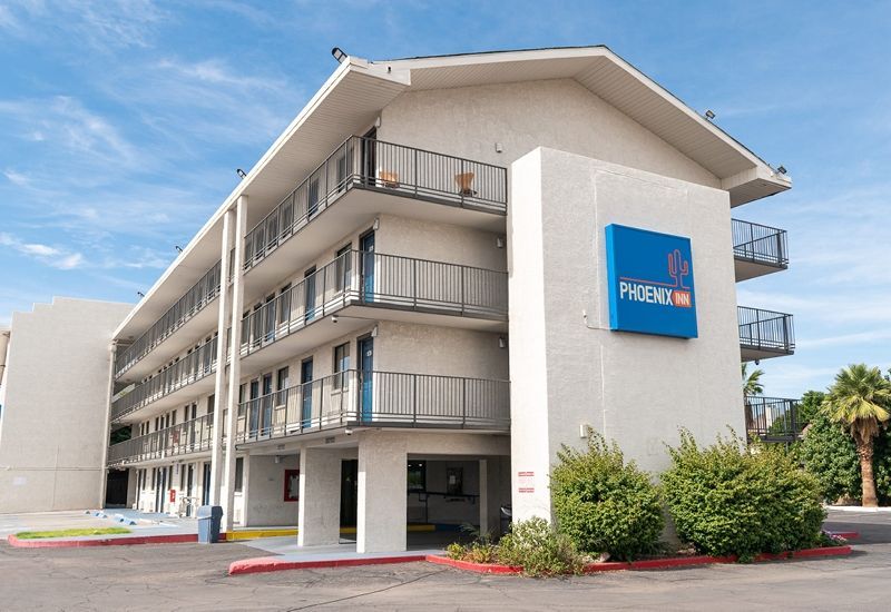 Three-story beige building with exterior walkways and balconies. Blue sign. Cloudy sky.
