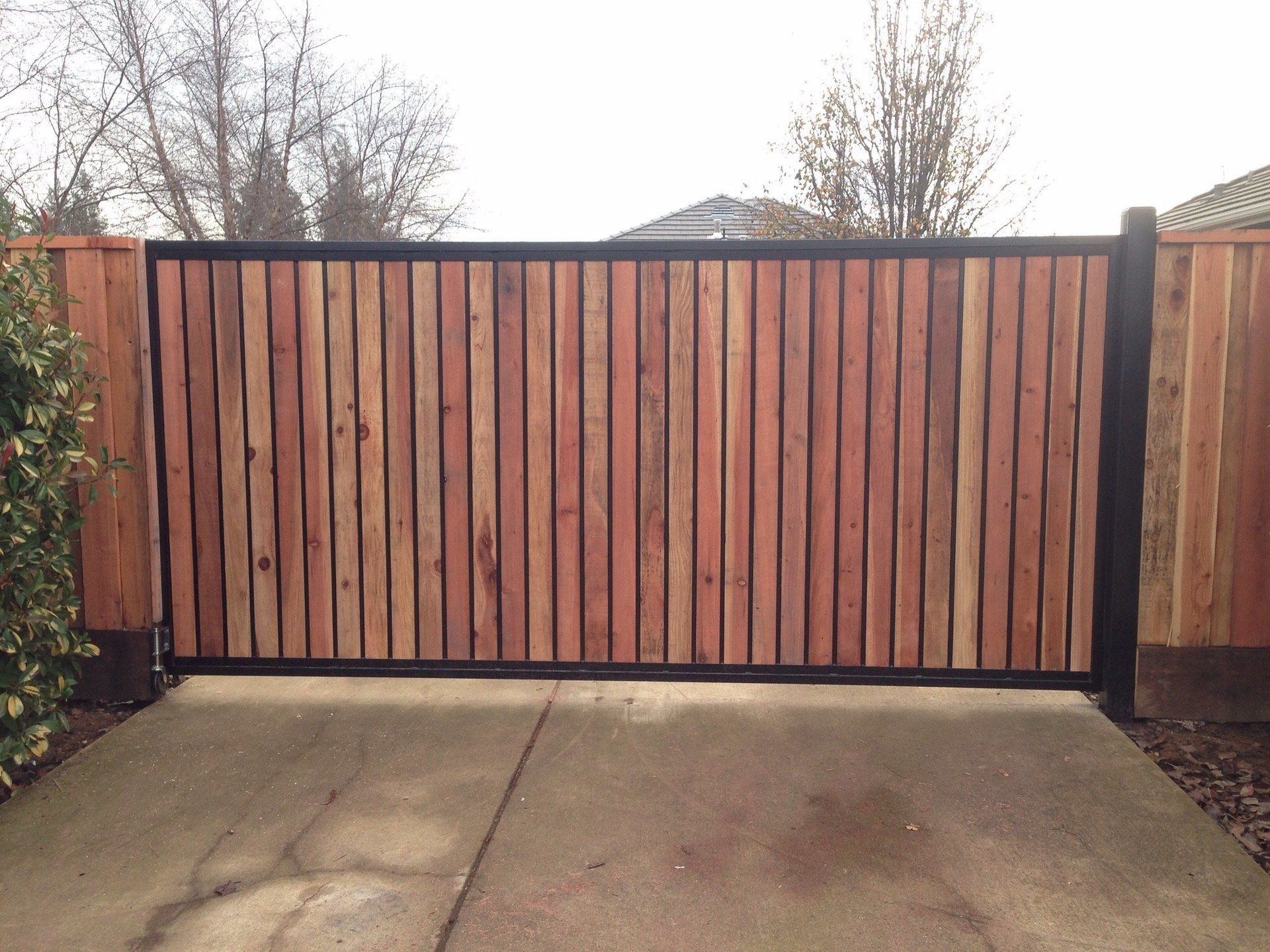 A wooden gate with a black frame is sitting on a concrete driveway.