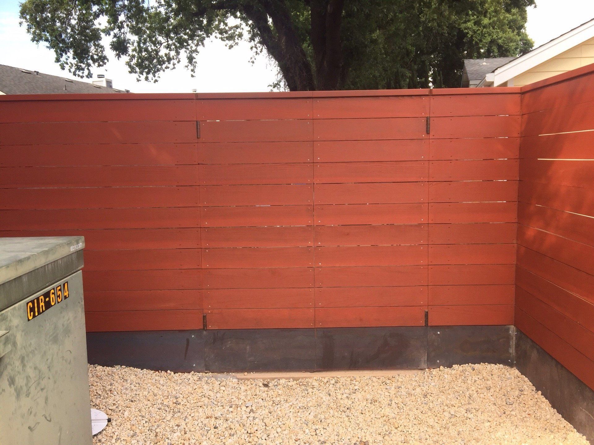 A red wooden fence surrounds a gravel area in a backyard.