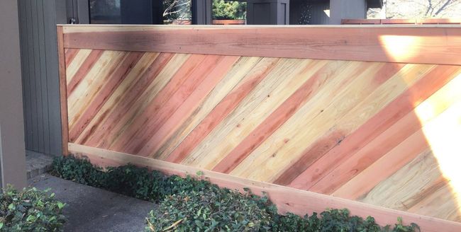 A wooden fence with a diagonal pattern is sitting next to a bush.