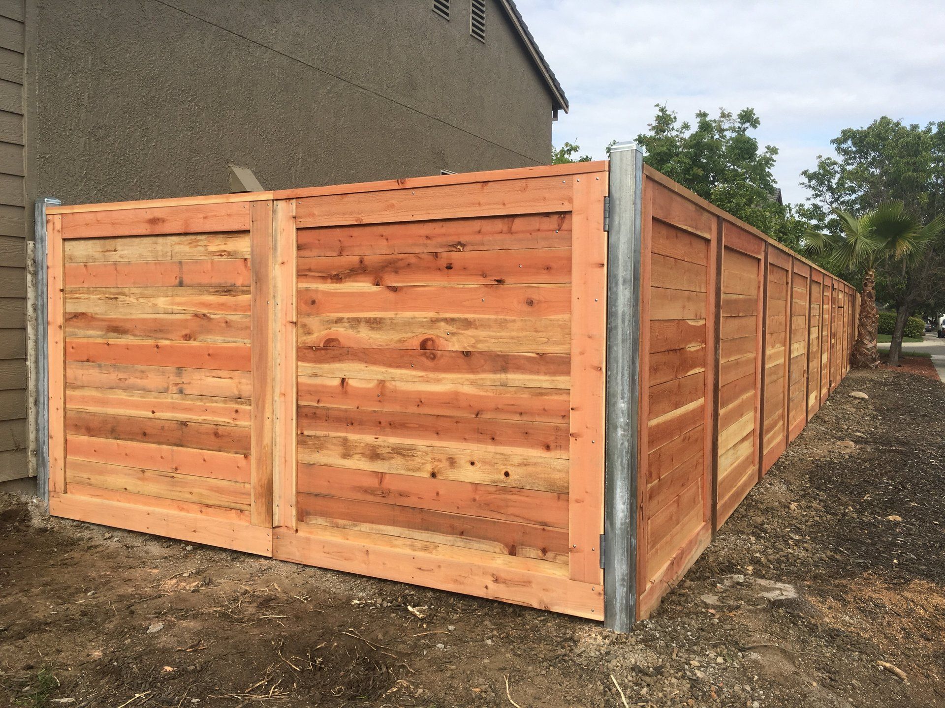 A wooden fence is sitting in the dirt in front of a house.