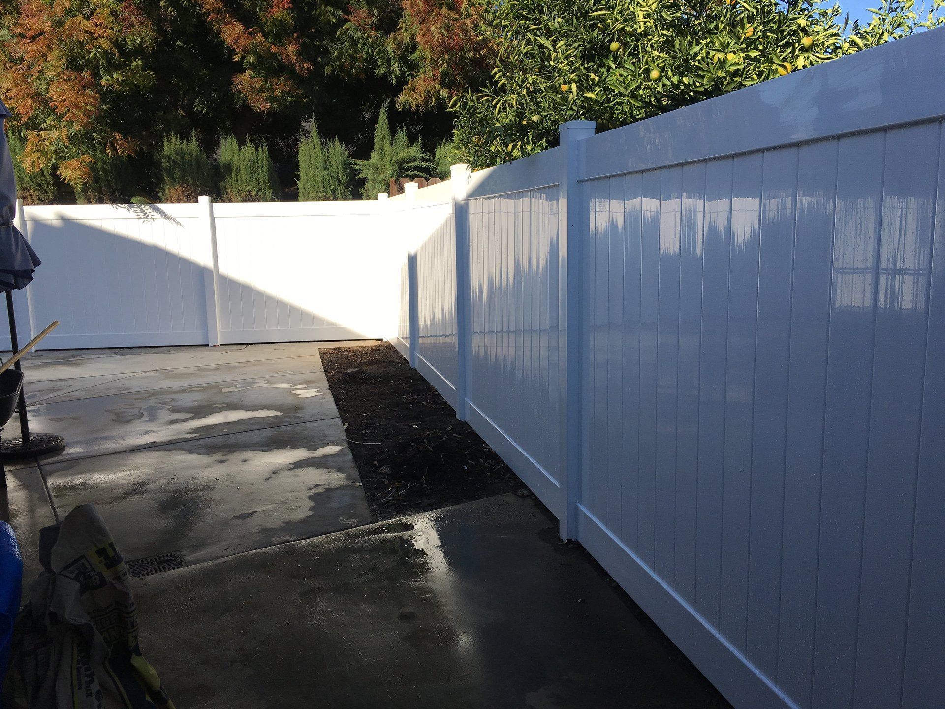 A white fence surrounds a concrete driveway with trees in the background